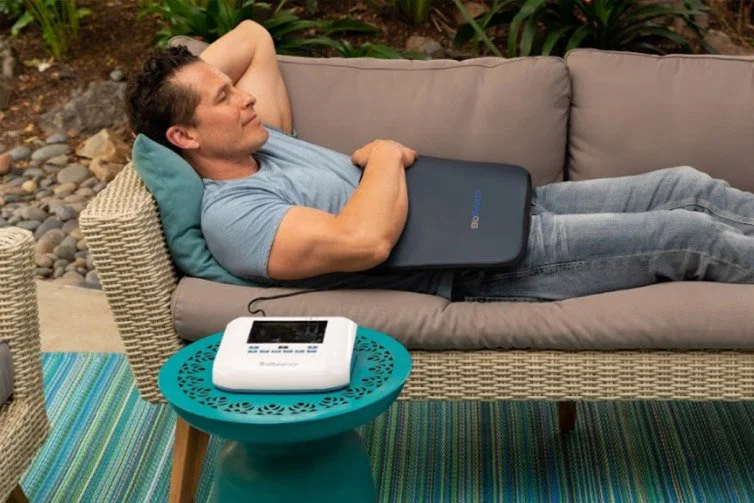Man lying down on couch while BioBalance PEMF machine is laid over his stomach