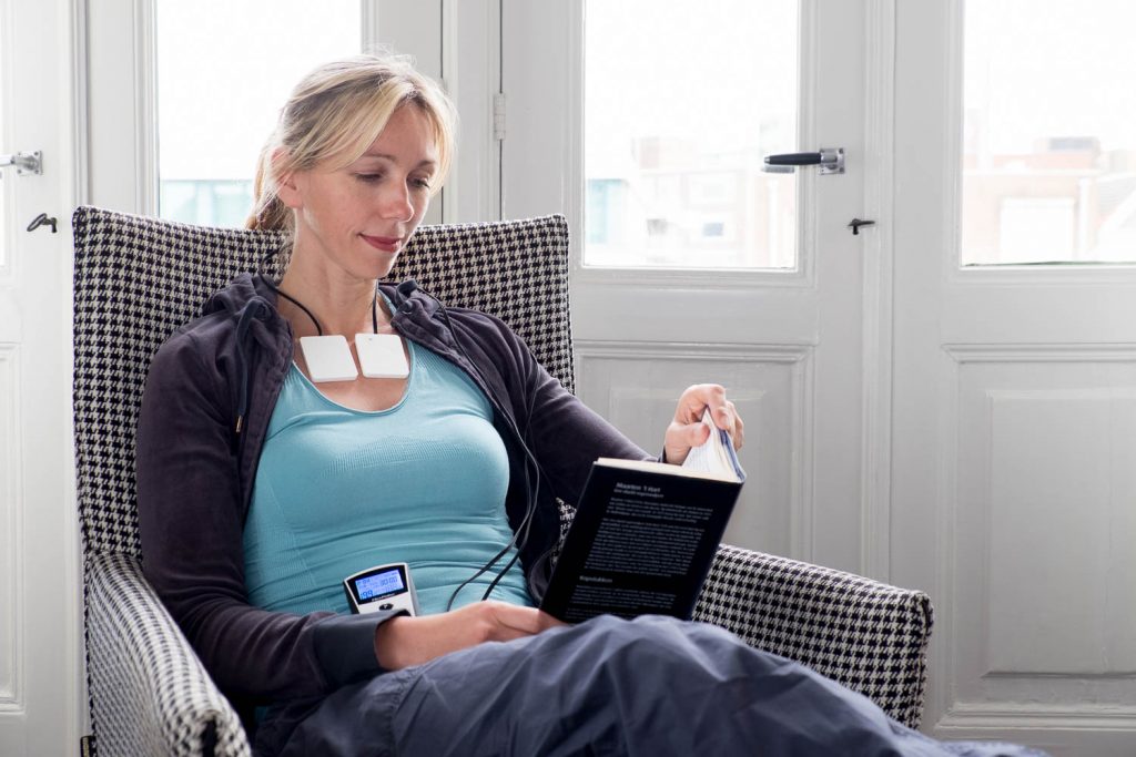 Woman sits and reads while PEMF device is being used right below her neck area, focusing on her thyroids.