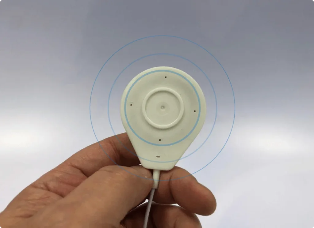 A hand holding a FlexPulse coil pad, with rings drawn around it to show the magnetic field reaching past the pad