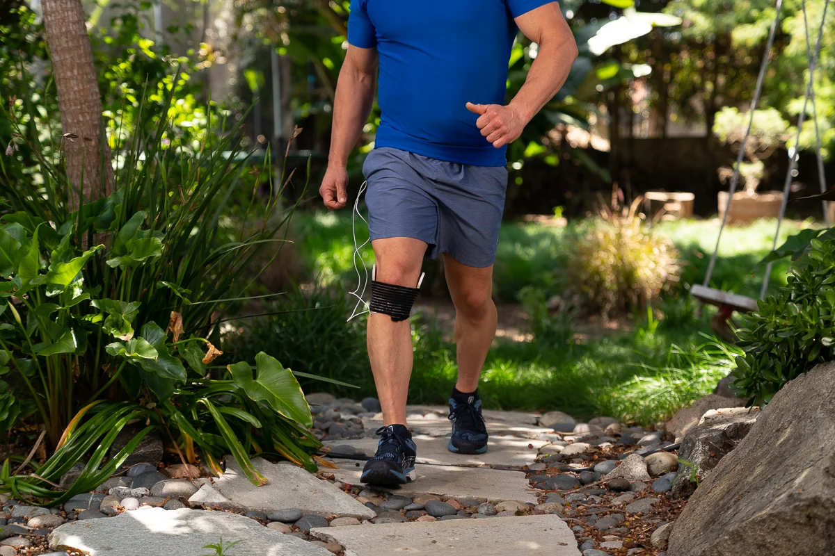 Athletic man walks through nature while PEMF device is wrapped around his knee area