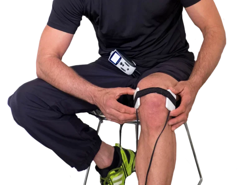 Man sits with FlexPulse device strapped to his shorts and PEMF coil pads applied to his knee