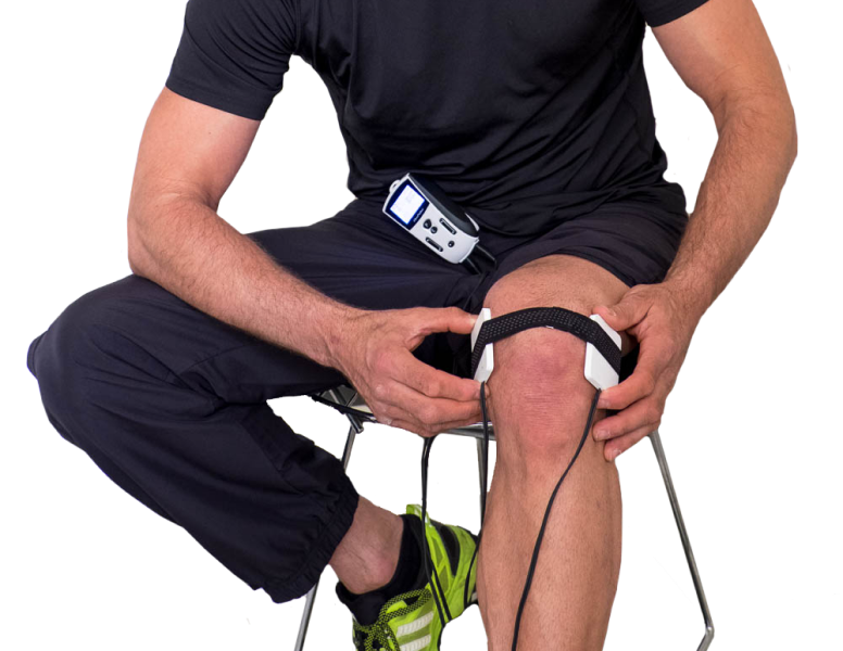 Man sits with FlexPulse device strapped to his shorts and PEMF treatment coils applied to his knee