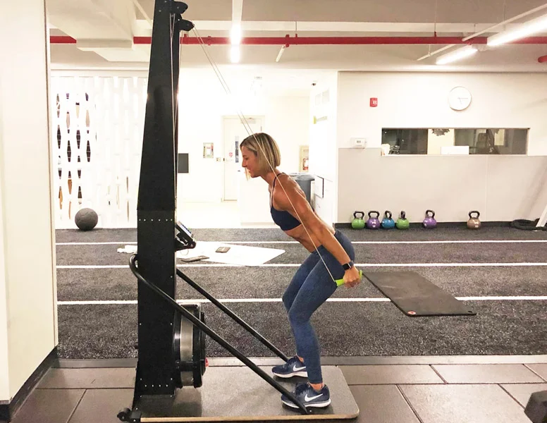 Woman in gym utilizing a pull down exercise and standing in a squatted position