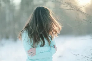 Girl outside seeming stressed and bundled up with her arms crossed at her chest