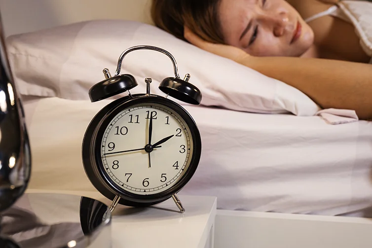 Woman lying stuck awake in bed with eyes wide open as the clock is approaching 2 in the morning