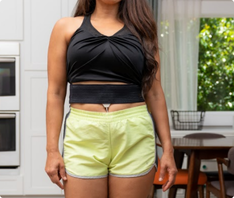 Coil pad on a woman’s stomach as she stands in her kitchen
