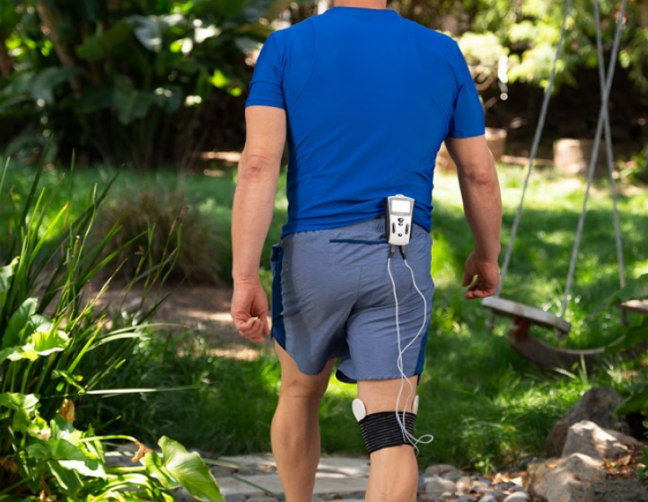 Man walking in nature with PEMF device on the back of his shorts and treatment coils running down to his knee.