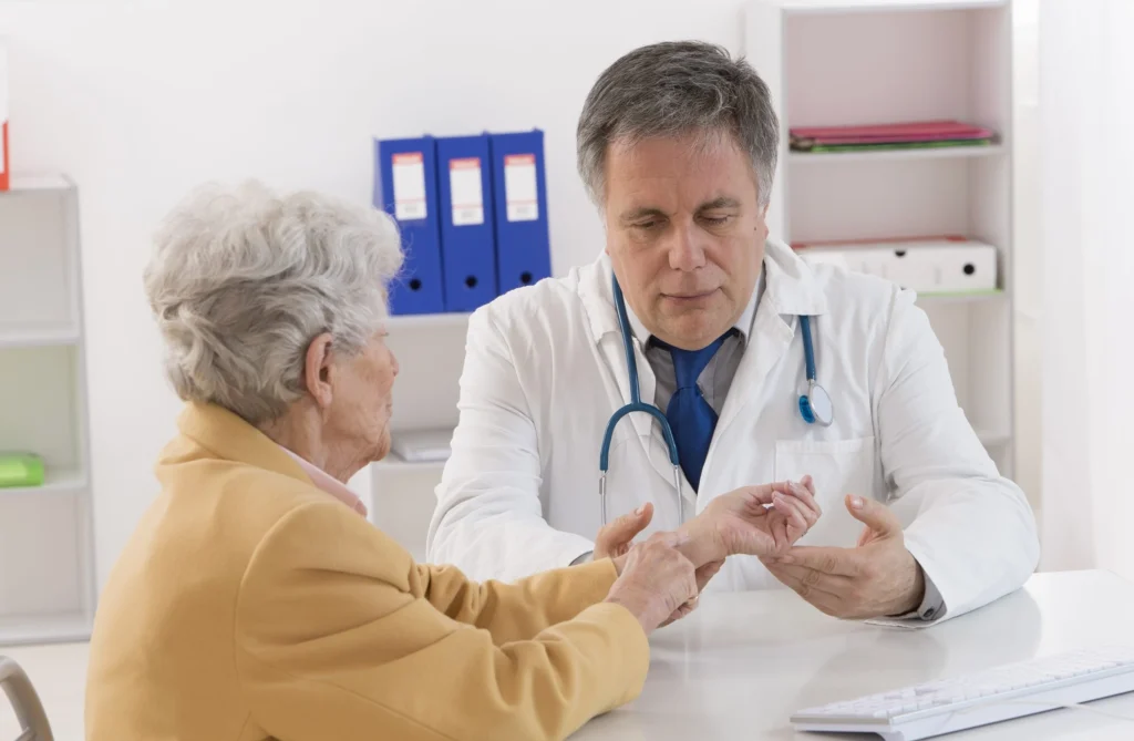 An elderly woman points to her wrist seemingly in pain as a doctor sits and listens to her problem.