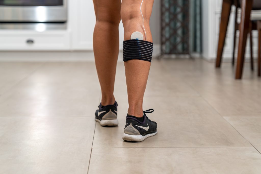 Legs of a woman in running shoes with a FlexPulse coil pad strapped to her calf