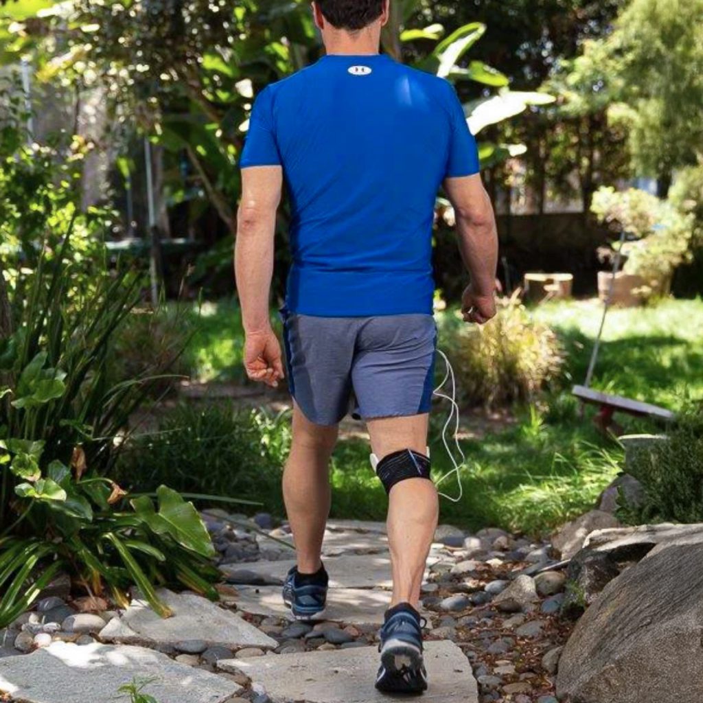 Person walking a garden path with a FlexPulse coil pad strapped to one knee