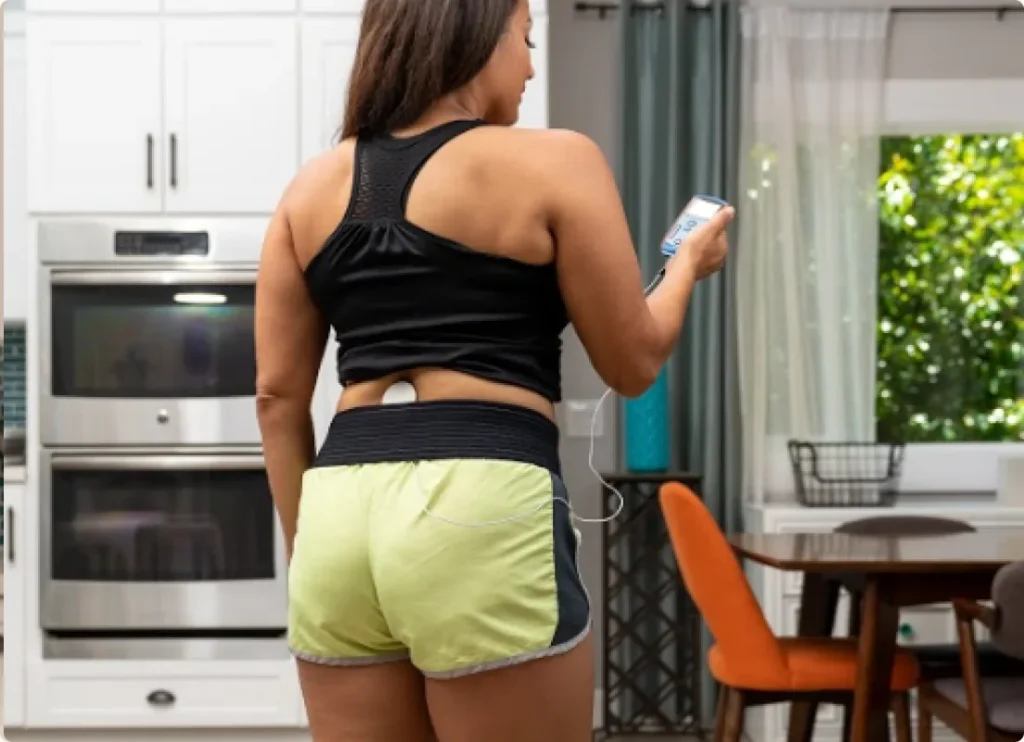 Woman in her kitchen holding the FlexPulse, a coil pad strapped to her lower back